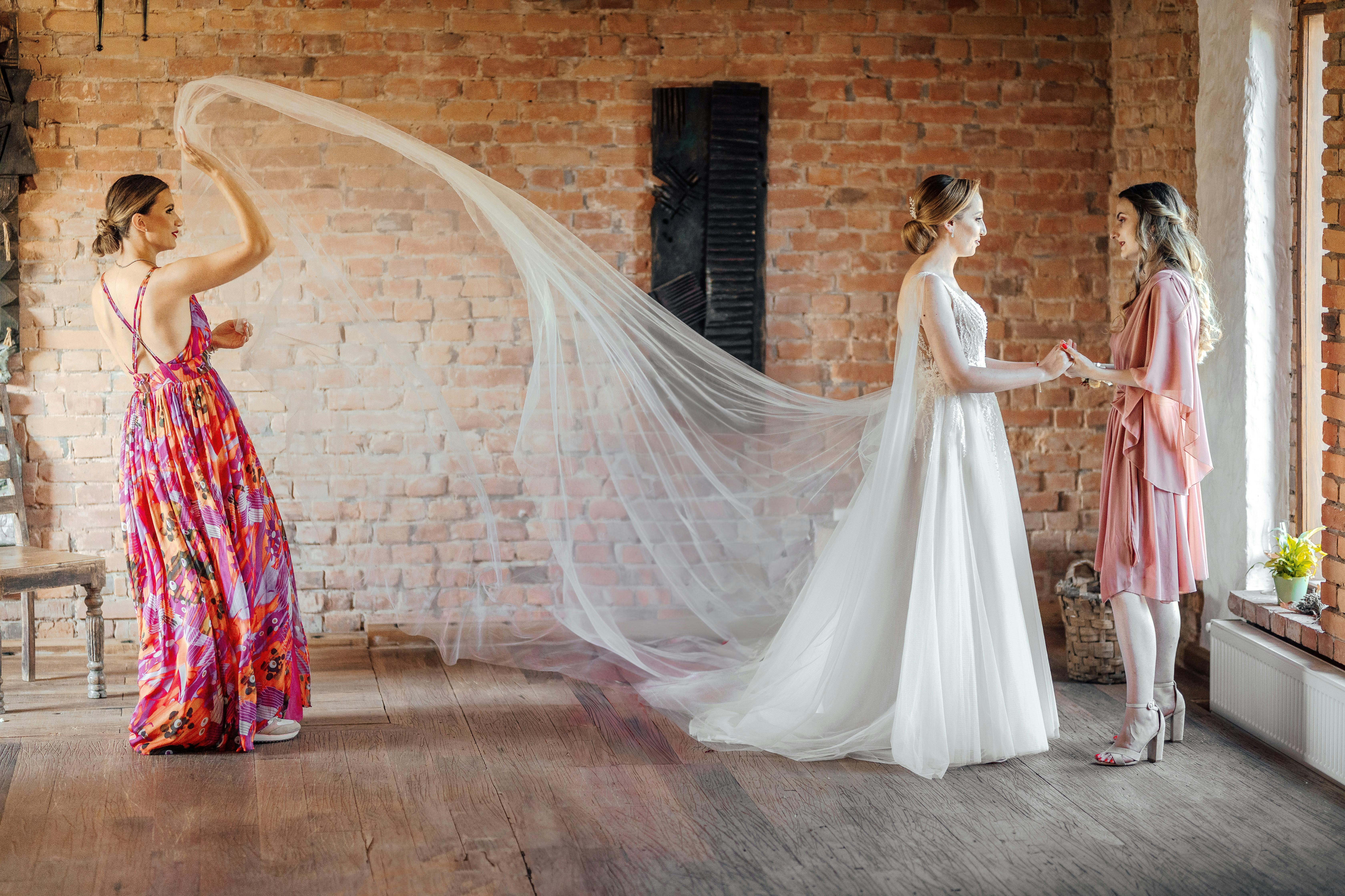 A bride in a wedding dress with bridesmaids in a rustic indoor setting, sharing a joyful moment.