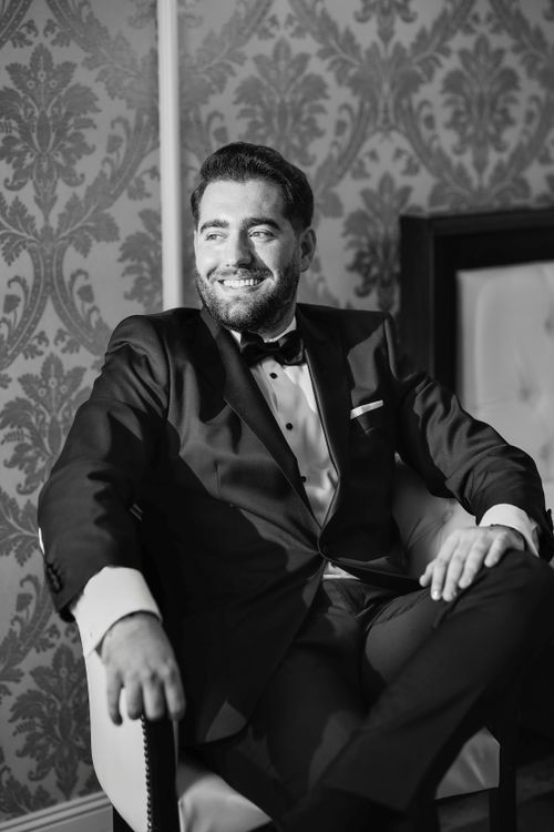 Free A groom in a tuxedo sitting confidently, captured in timeless black and white. Stock Photo