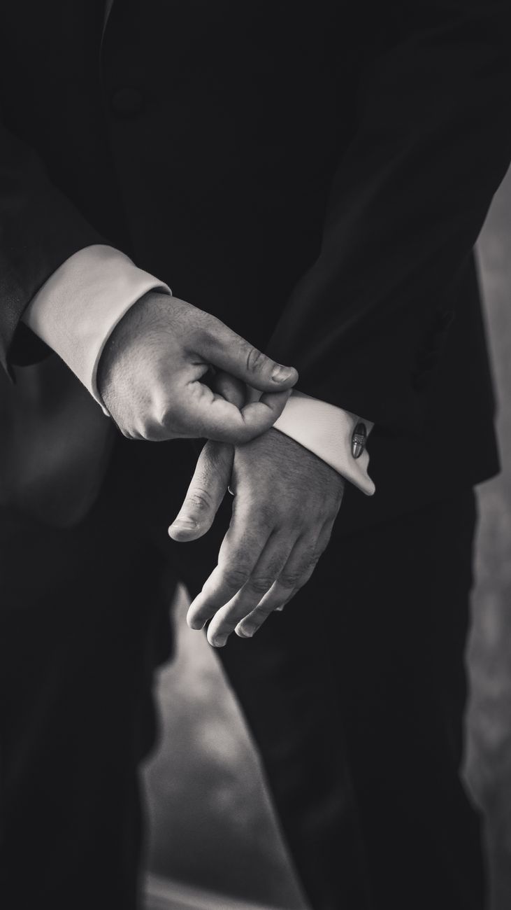 A close-up black and white photo of a man adjusting his cufflinks on a formal suit.