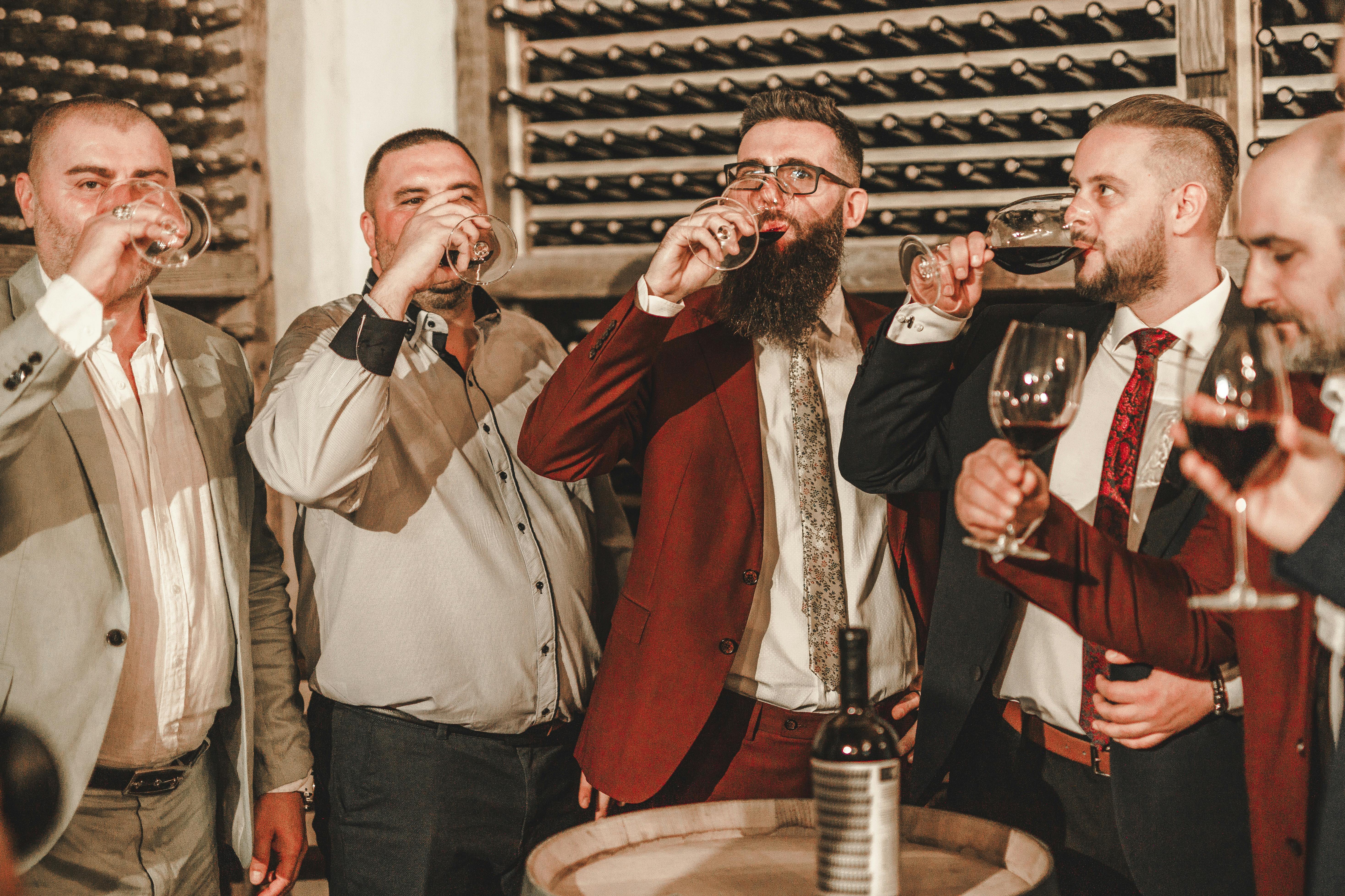Group of men in suits drinking wine at an indoor winery gathering.
