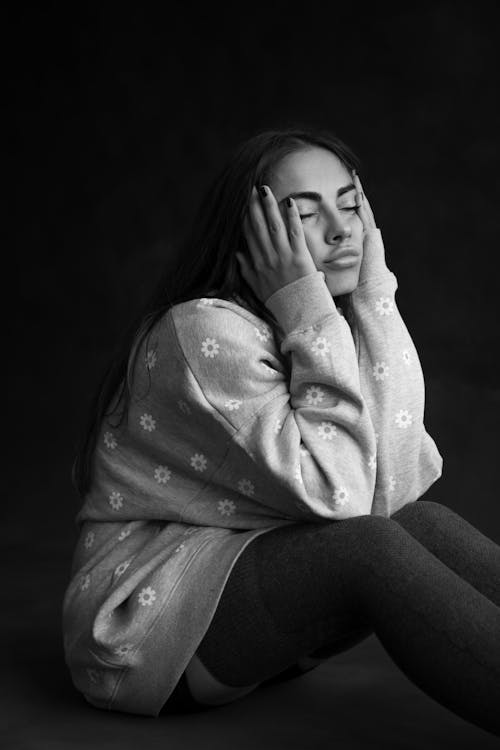 Woman Sitting with Eyes Closed and Hands on Cheeks