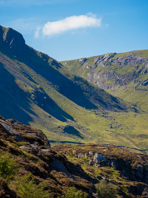 Free A breathtaking view of a sunlit mountain valley with grassy slopes under a clear blue sky. Stock Photo