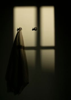 A towel hangs in soft sunlight, casting dramatic window shadows on the wall.