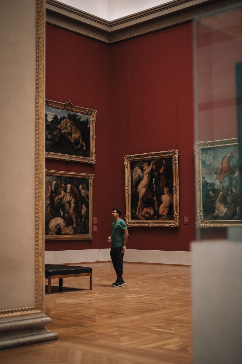 A visitor looking at classic oil paintings hung on a red gallery wall.