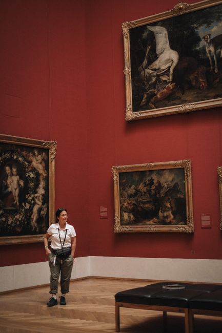 A woman standing in an art museum in Munich, Germany, observing classical paintings on the wall.