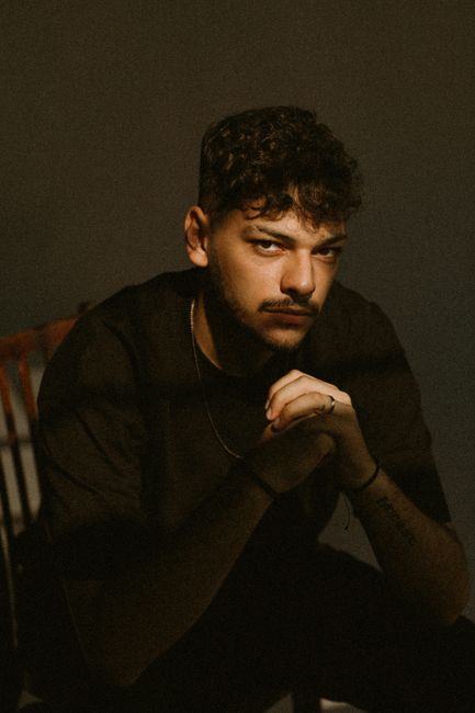 Intense portrait capturing a young man with curly hair sitting indoors, exuding a dark and moody vibe.