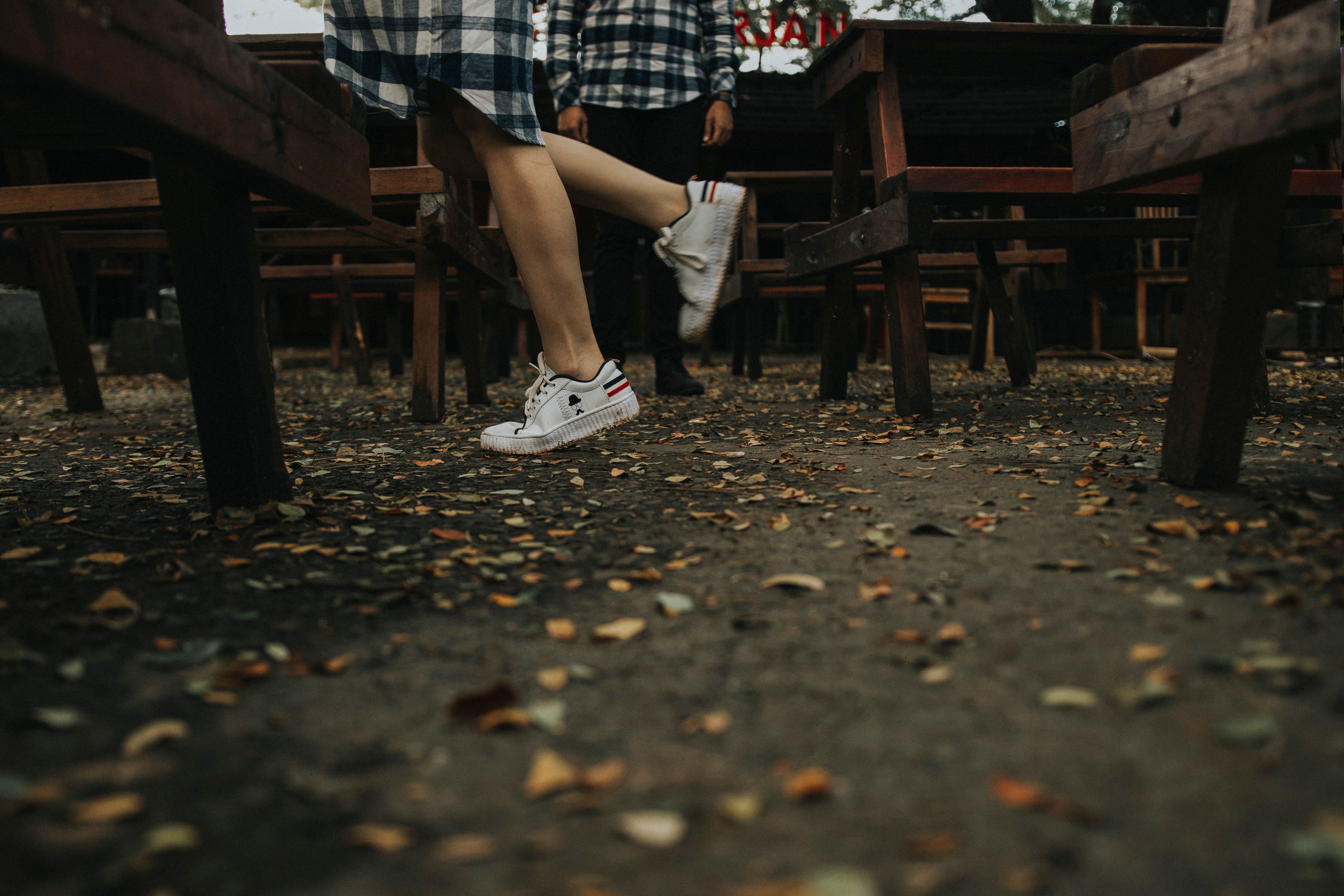 A person wearing sneakers walks through fallen leaves and wooden benches in an outdoor setting, capturing an autumn vibe.