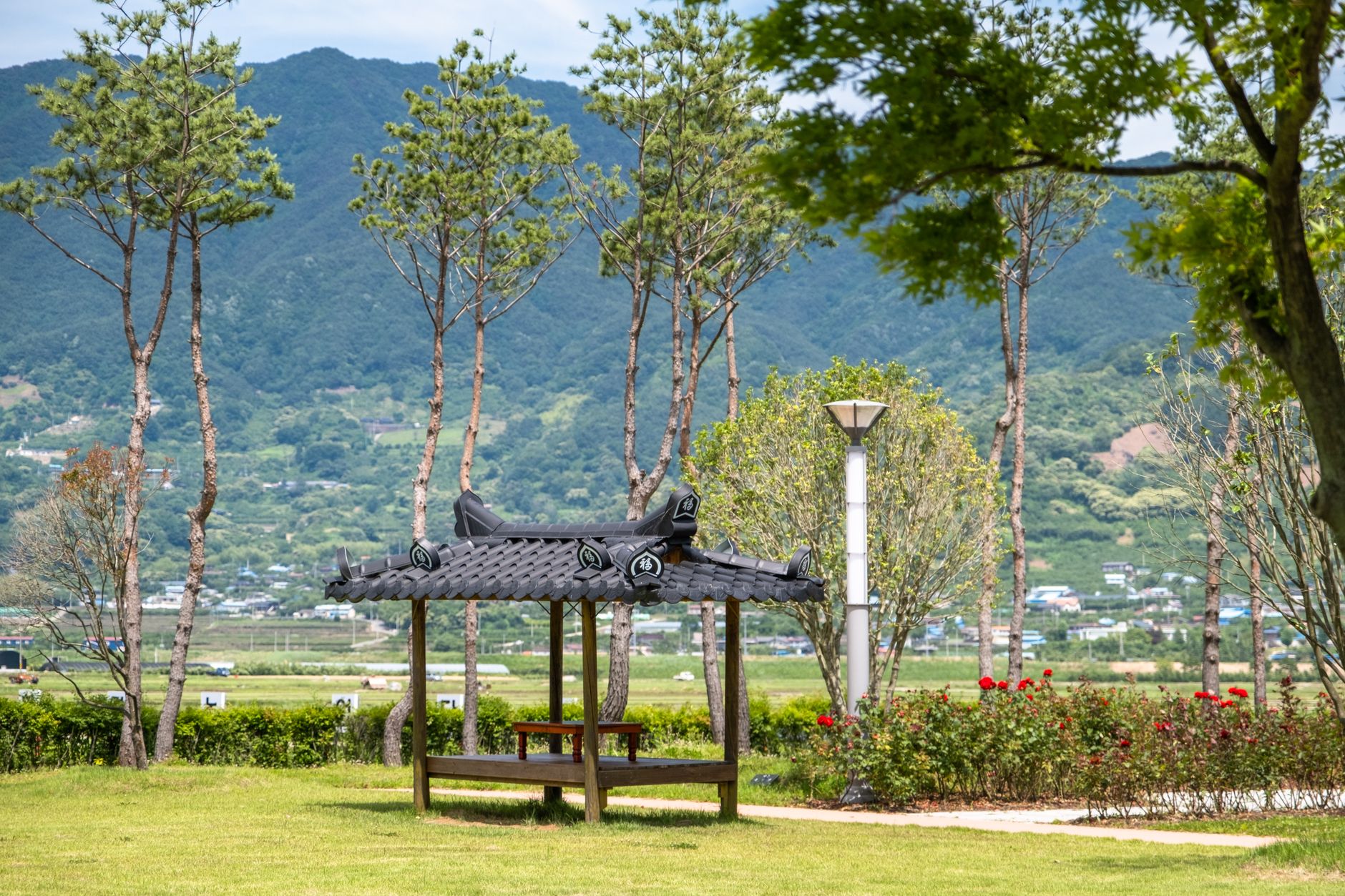 Scenic view of a traditional pavilion in a peaceful park setting with mountains.