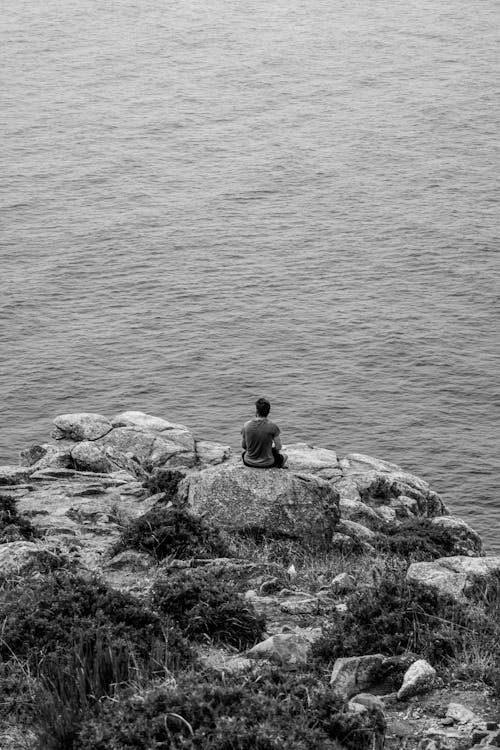 Free Man Sitting on Rocks on Sea Shore Stock Photo