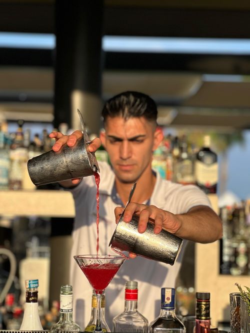 Free A bartender skillfully pours a red cocktail at an outdoor bar, showcasing mixology expertise. Stock Photo