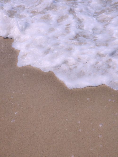 Free Close-up of foamy sea waves softly washing over sandy beach, capturing tranquil nature. Stock Photo