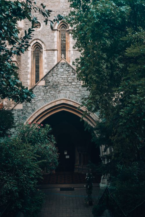 Free A serene view of a Gothic church entrance framed by lush greenery, showcasing architectural beauty. Stock Photo