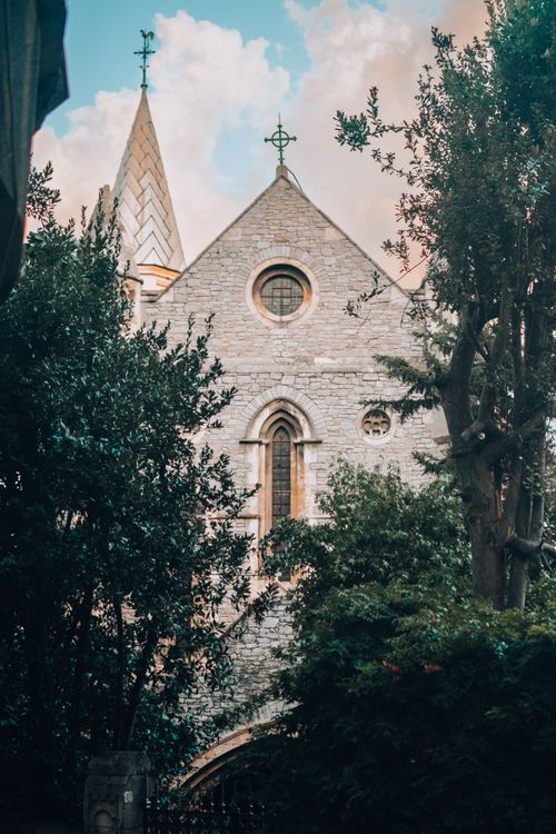 Free A historic church facade surrounded by lush trees under a bright sky, creating a serene scene. Stock Photo