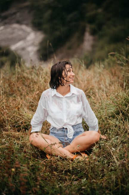 A woman sits cross-legged in a grassy field, enjoying a serene moment in nature.