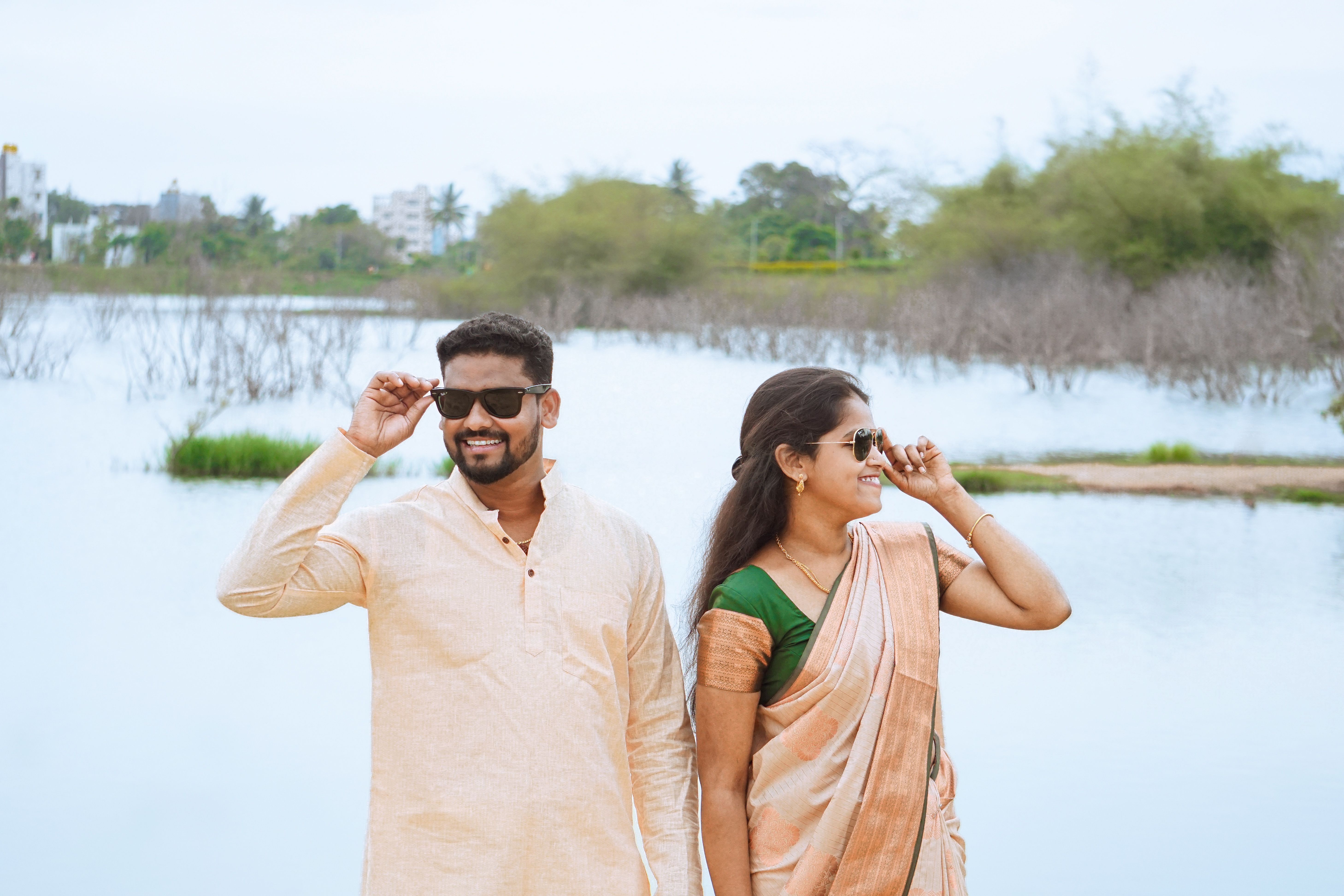 Smiling couple in traditional clothing enjoying a sunny day by the lake.