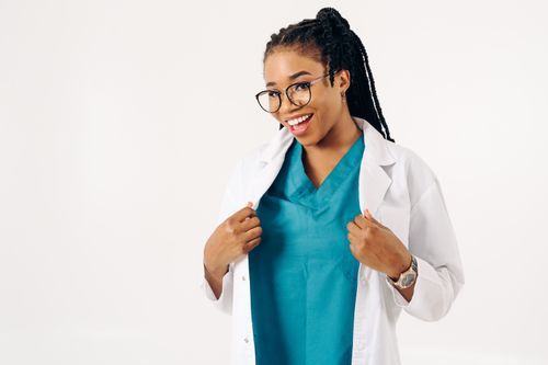 Free Confident female doctor smiling in a white coat with teal scrubs, embodying professionalism and approachability. Stock Photo