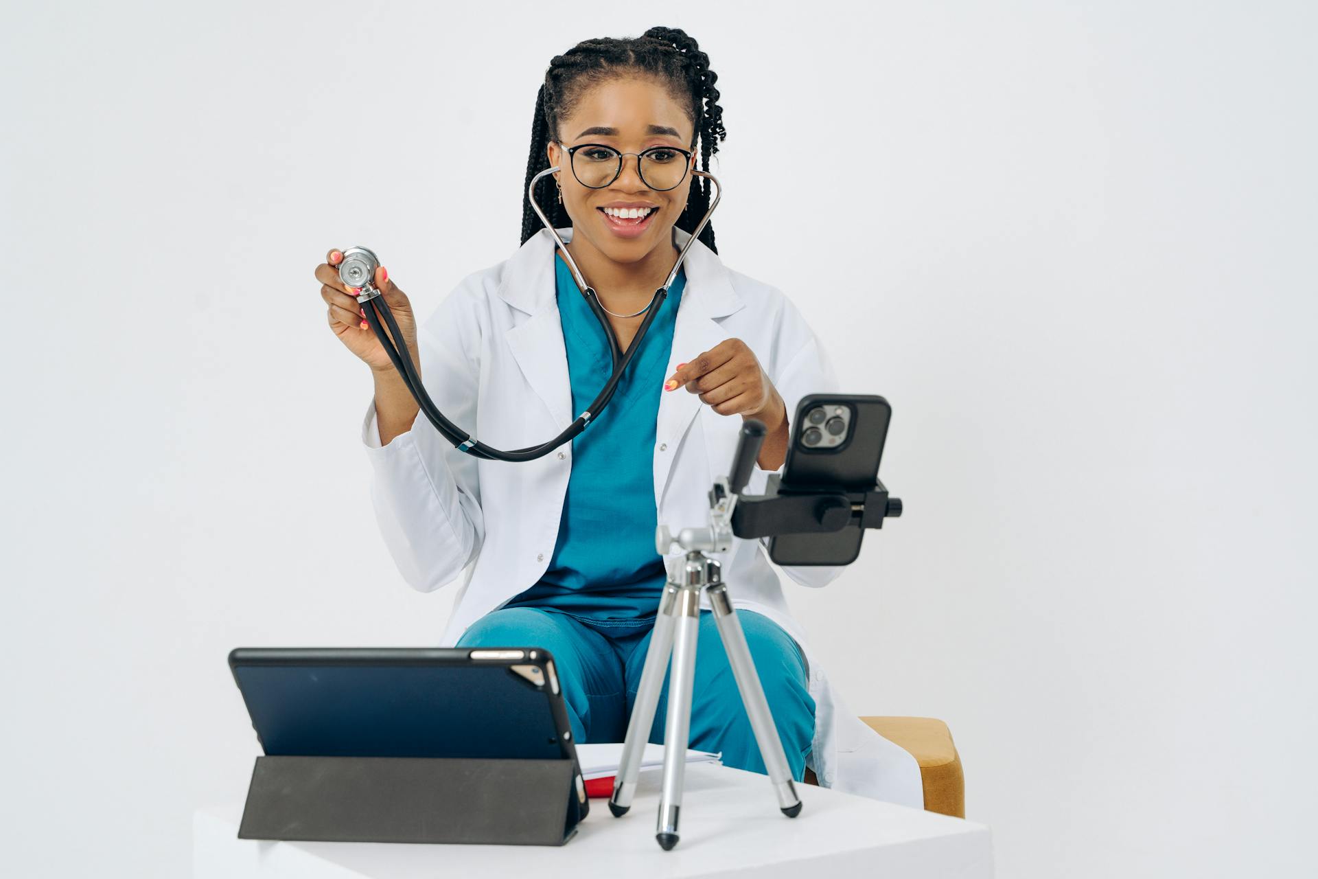 A smiling female doctor conducting a telehealth consultation using a smartphone and tablet.