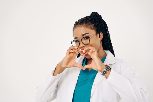 Free A friendly doctor in a white coat making a heart gesture with her hands, symbolizing care. Stock Photo