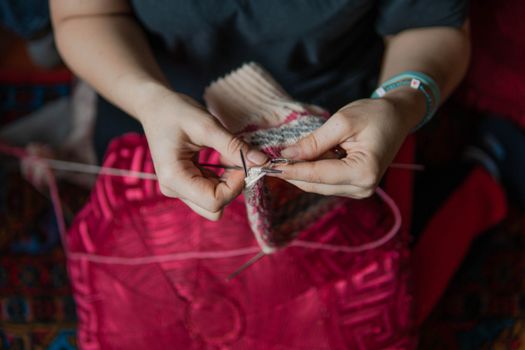 Detail shot of hands knitting with red wool, showcasing traditional craftsmanship and creativity.
