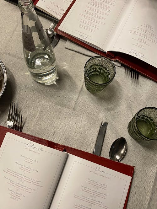 Open Menu, Glasses, Bottle of Water and Cutlery on Gray Tablecloth
