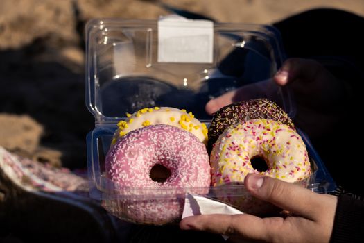 A close-up of colorful donuts in a plastic box, perfect for a sweet treat on the beach.