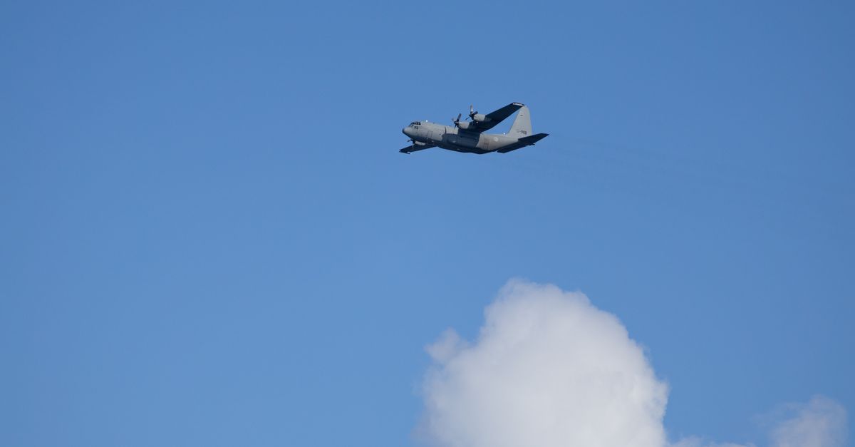 Lockheed C-130 Hercules aircraft flying against a clear blue sky with clouds.