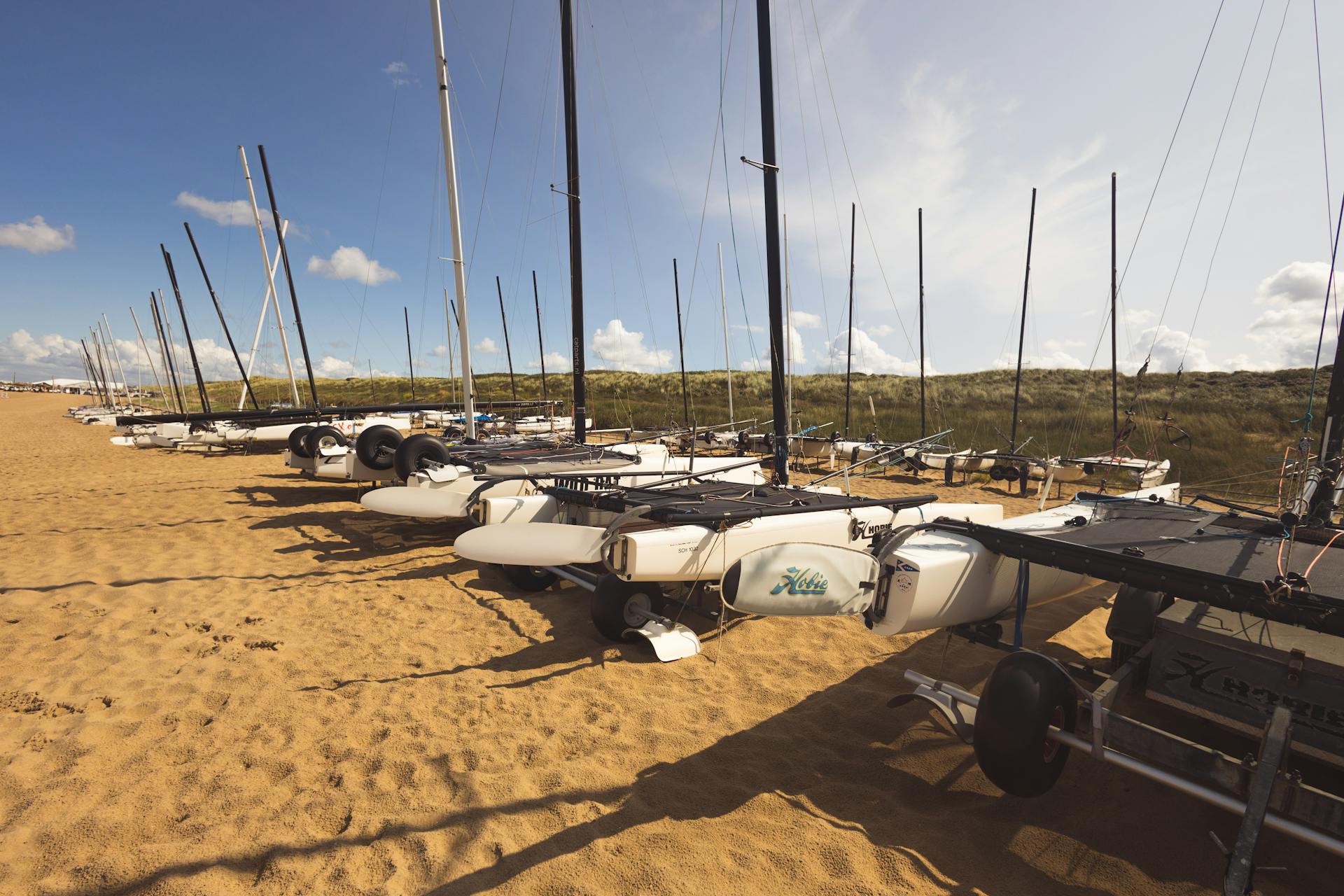 Catamarans on a sandy beach ready for sailing under a bright blue sky.