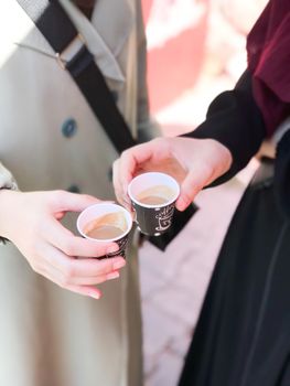 Two individuals holding espresso cups on a sunny city street, sharing a coffee moment.