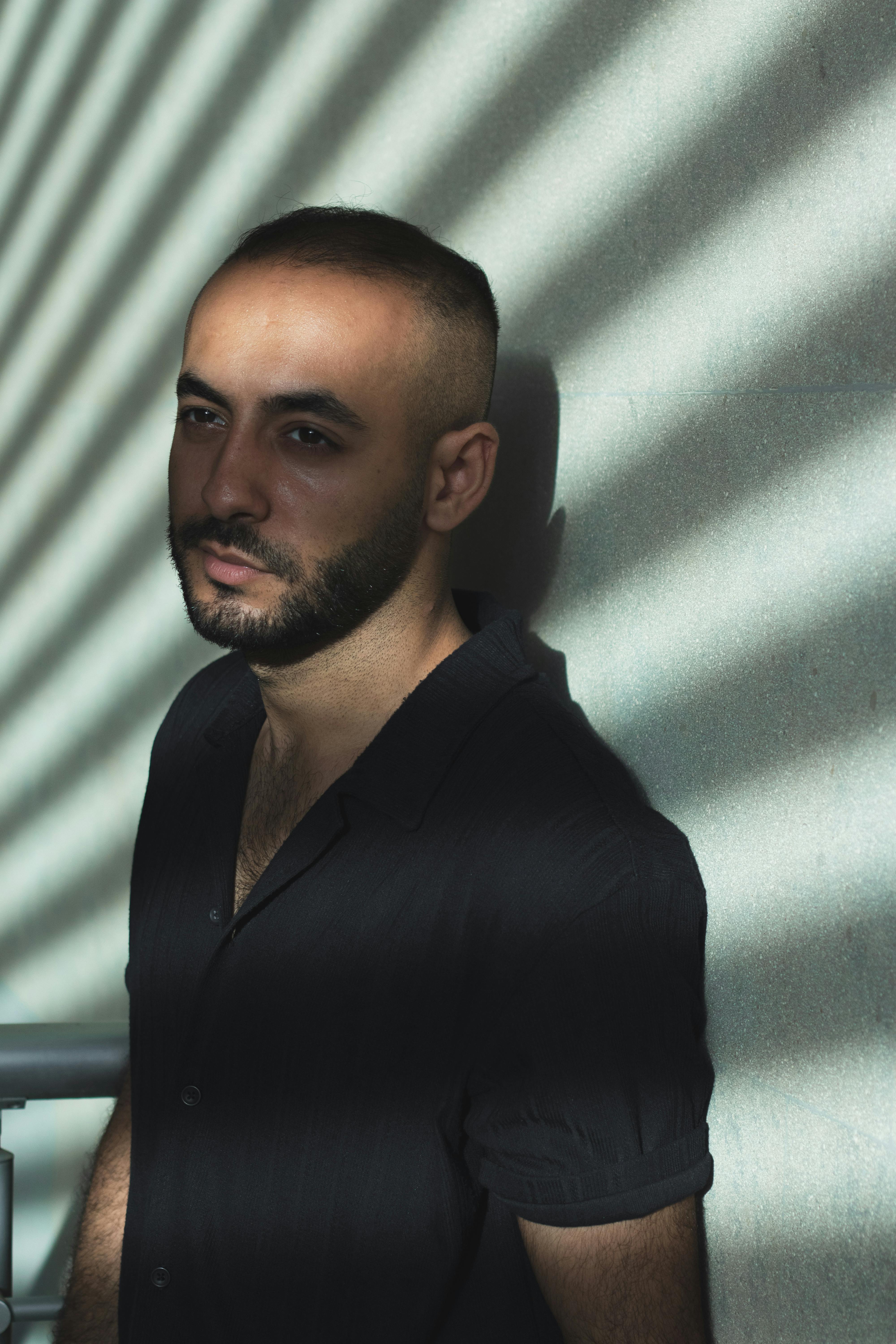 Man standing against a wall with dramatic striped shadows. Indoor portrait with a contemplative mood.