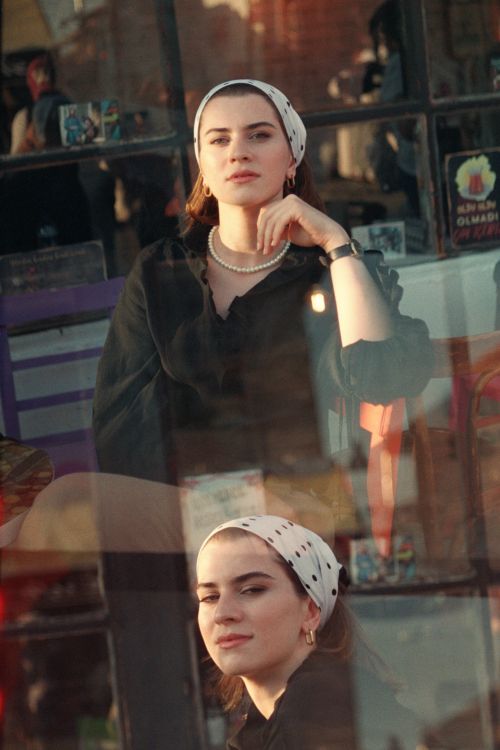 Free Elegant double exposure portrait of a young woman sitting outdoors with reflective glass effect. Stock Photo