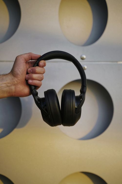 Free A close-up of a hand holding black wireless headphones against a modern geometric background in Kyiv. Stock Photo