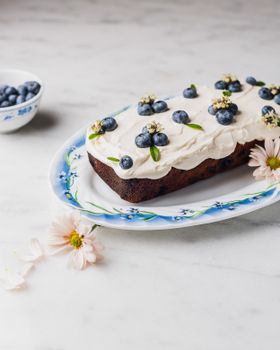 Delicious blueberry cake topped with cream frosting and flowers, set on a floral plate.