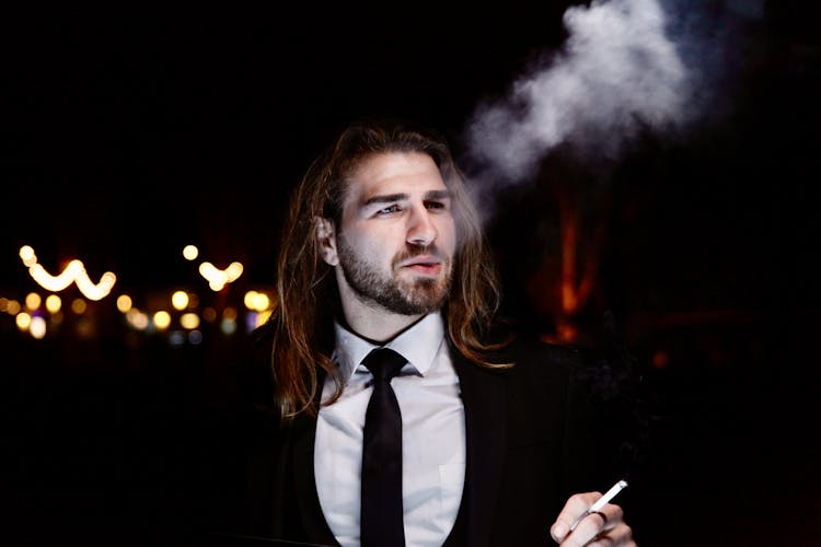 Man With Long Hair In Suit Smoking In Dark