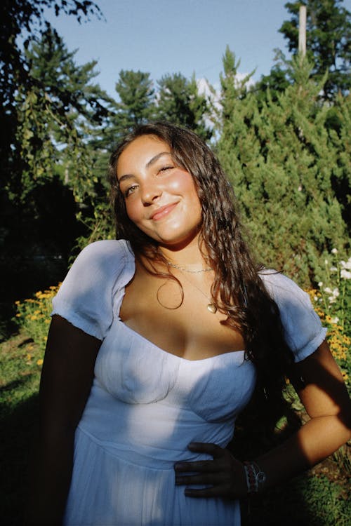 Young Brunette in a White Dress Standing Outside in Sunlight 