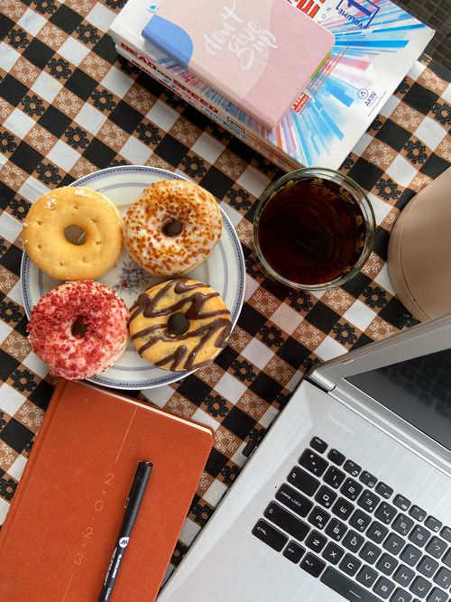 Free Four donuts on a plate with iced coffee beside a laptop on a checkered table. Stock Photo