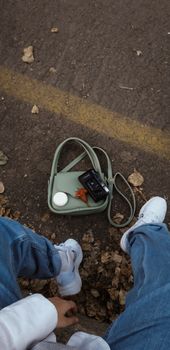 Casual street style featuring jeans, sneakers, and a purse on a road with fallen leaves.