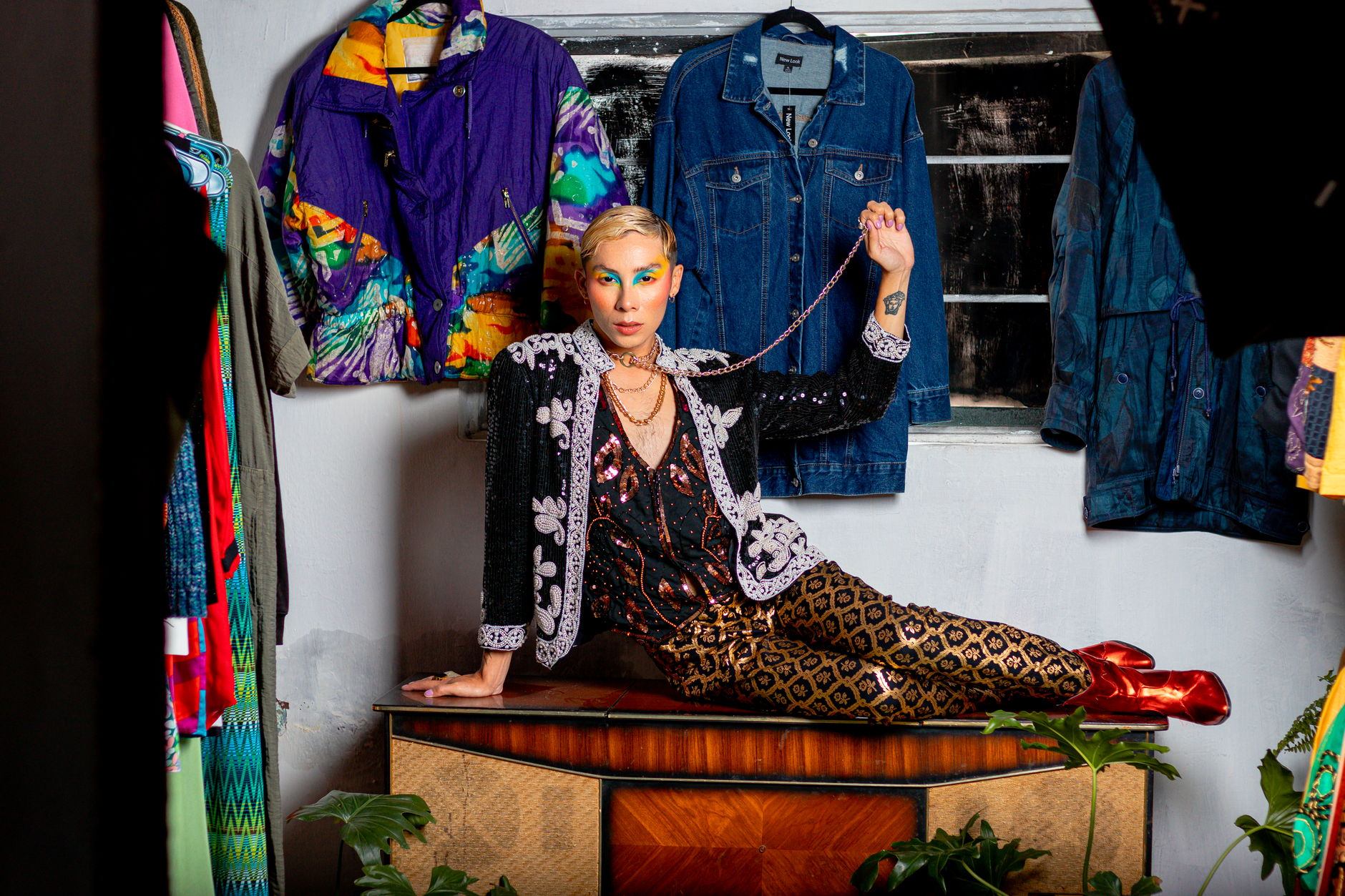 Stylish model posing confidently in eclectic retro outfits with vibrant makeup in a fashion studio setting.