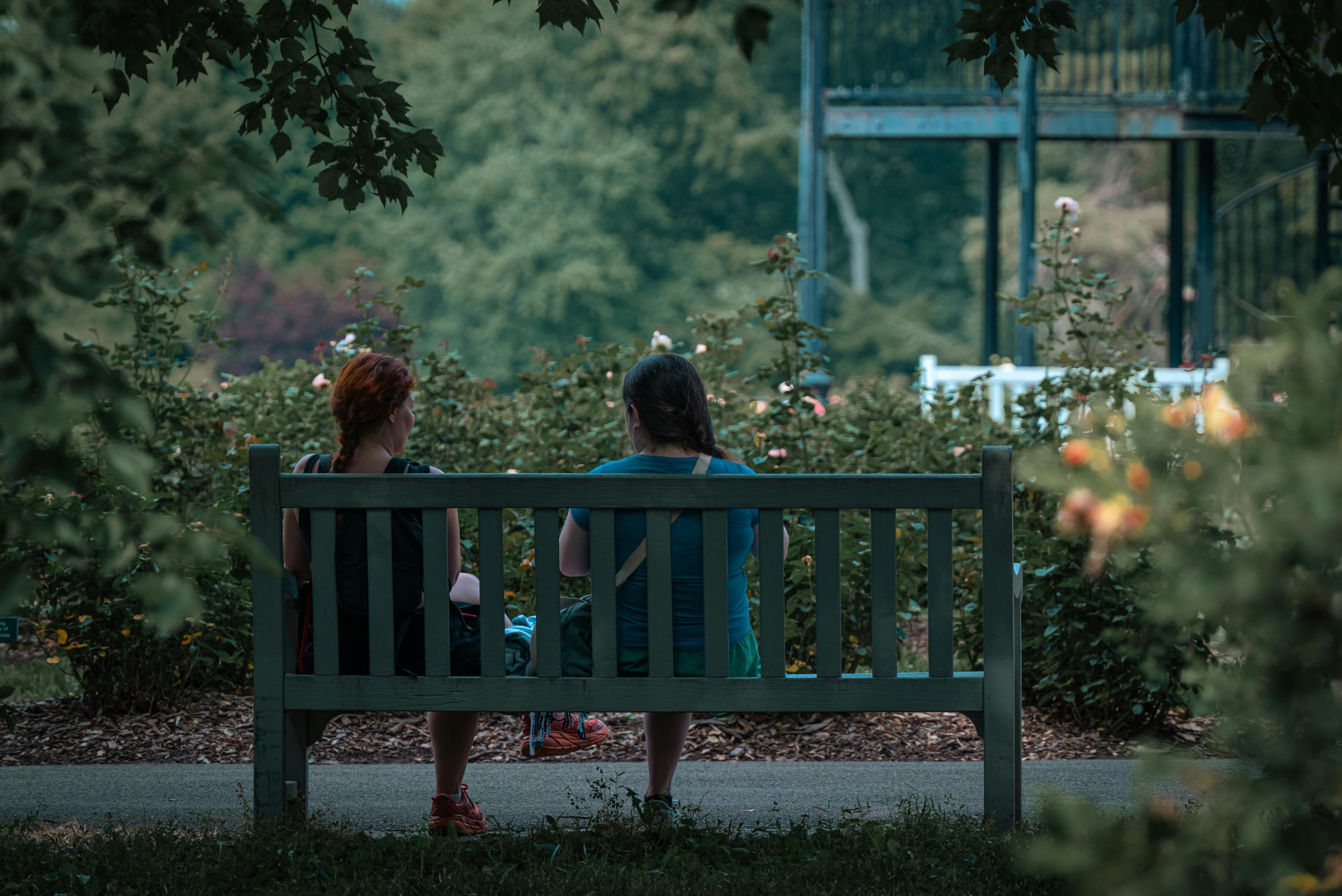 Girl sitting on wooden bench outside in a green park looking at