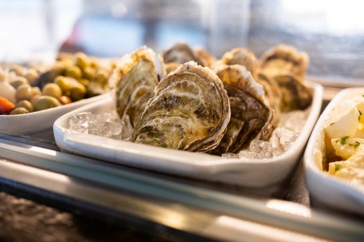 Plate of fresh oysters on ice with olives and potato salad, perfect for seafood lovers.