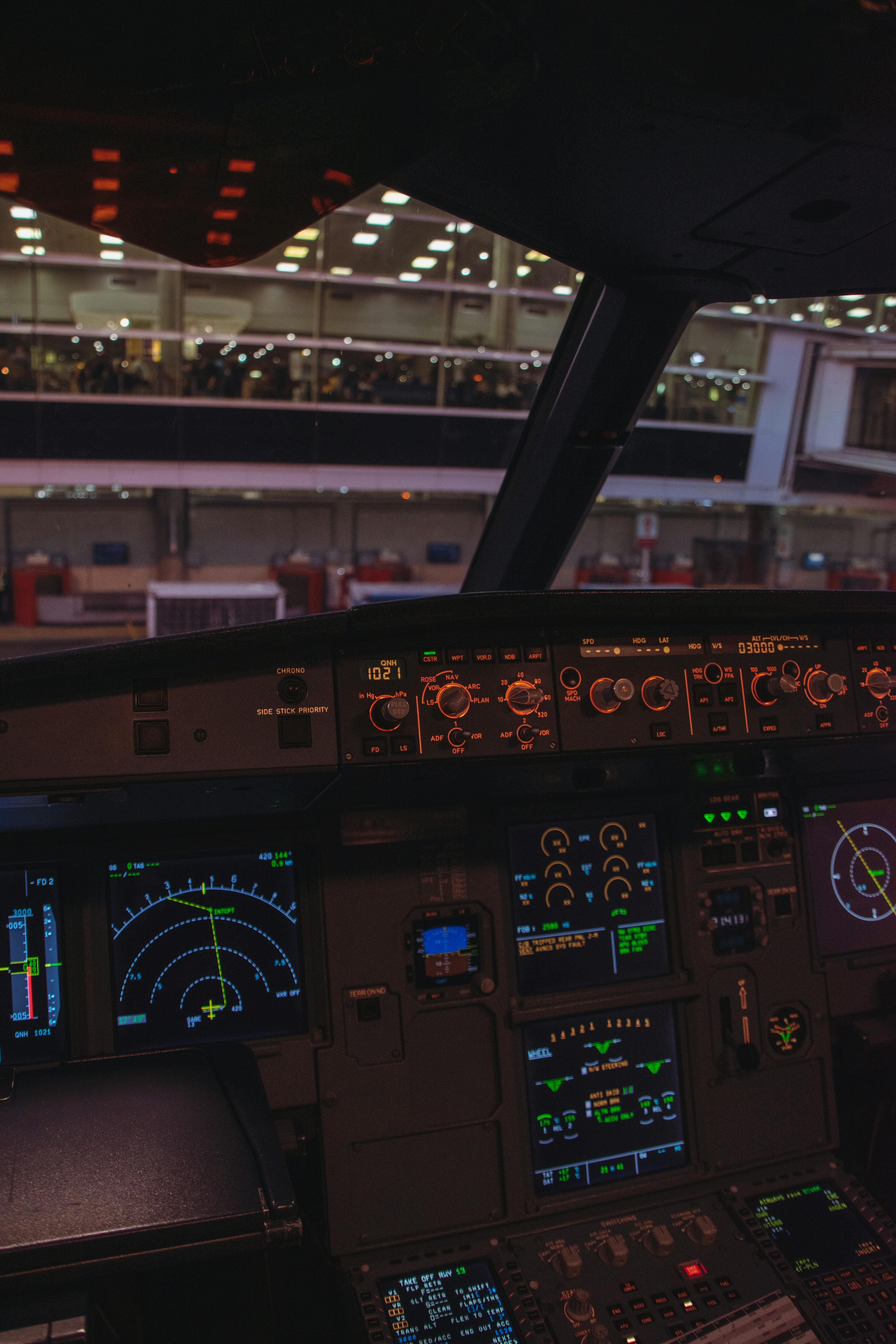 View from an airplane cockpit looking out onto an airport at night. Illuminated control panels add a dramatic feel.
