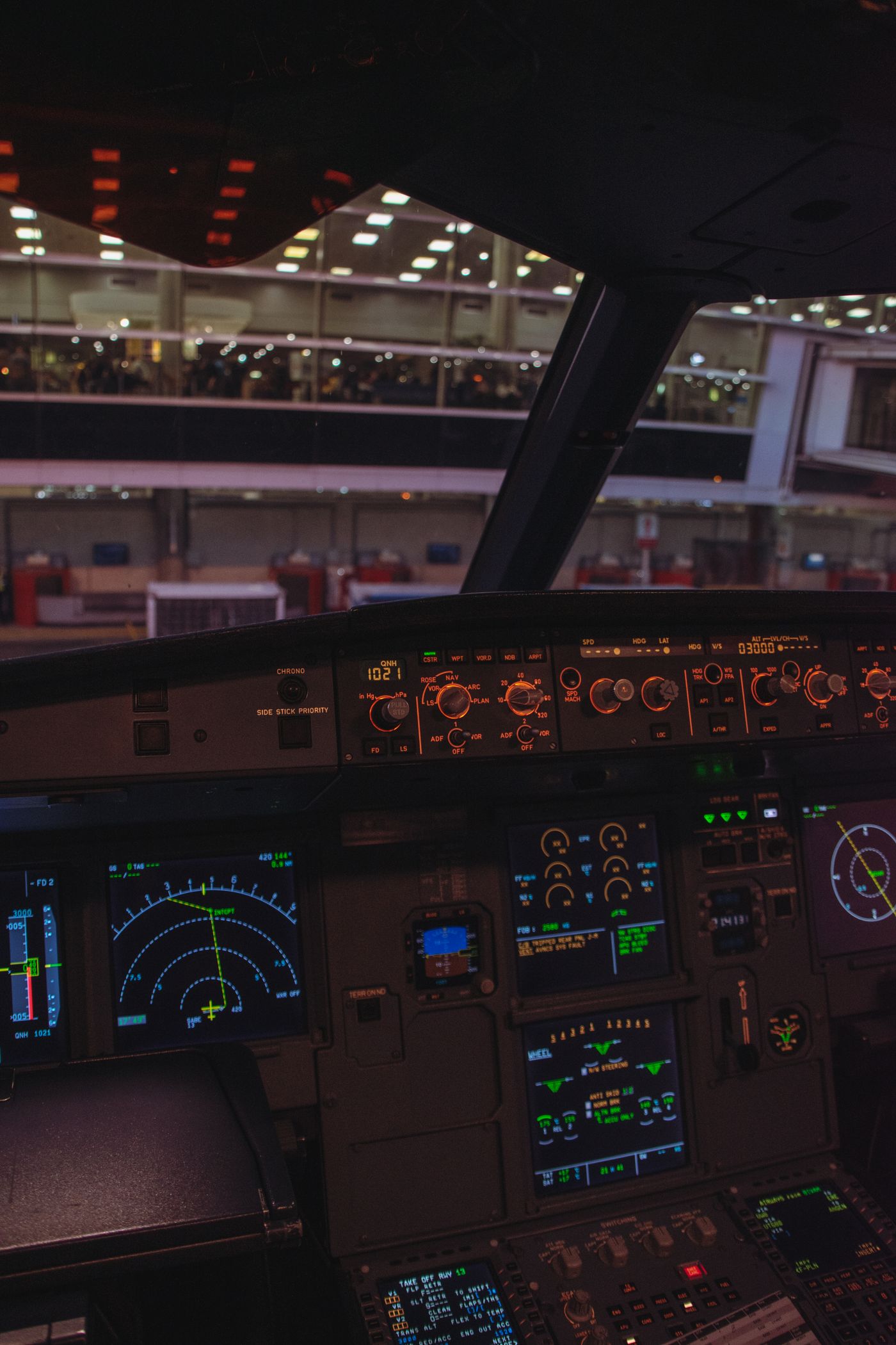 View from an airplane cockpit looking out onto an airport at night with illuminated control panels