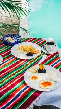 Colorful breakfast table with Mexican decor by a pool, featuring eggs and coffee.