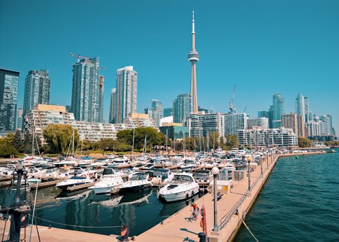 Vibrant view of Toronto's skyline with CN Tower, focusing on a bustling harbor with boats and skyscrapers.