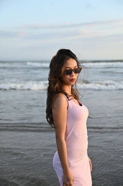 Stylish woman in sunglasses stands on Denpasar beach, embracing the sunset.
