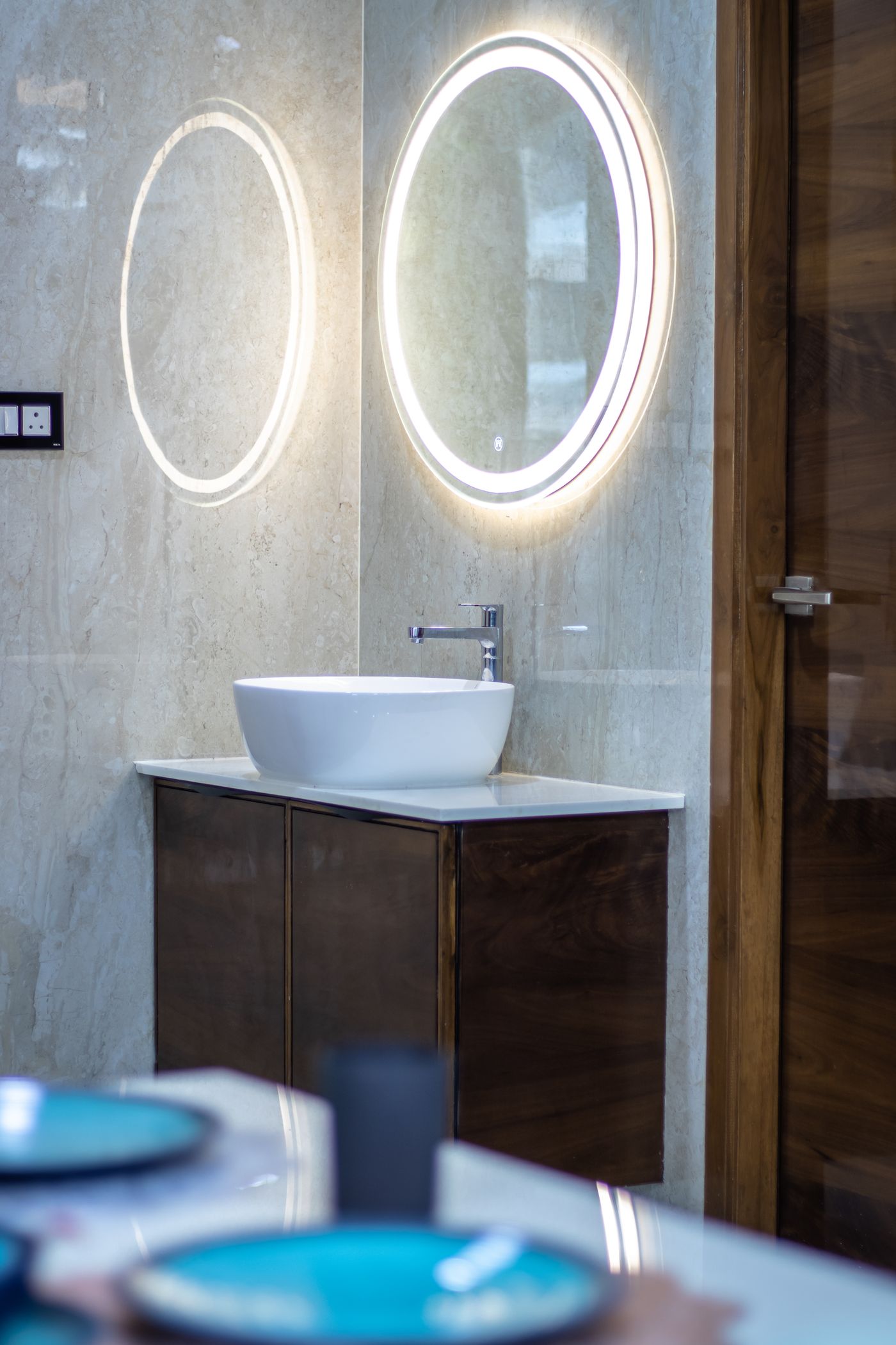 Bathroom vanity with dark timber cabinetry, white vessel basin, chrome tap, illuminated oval mirror, and timber door.
