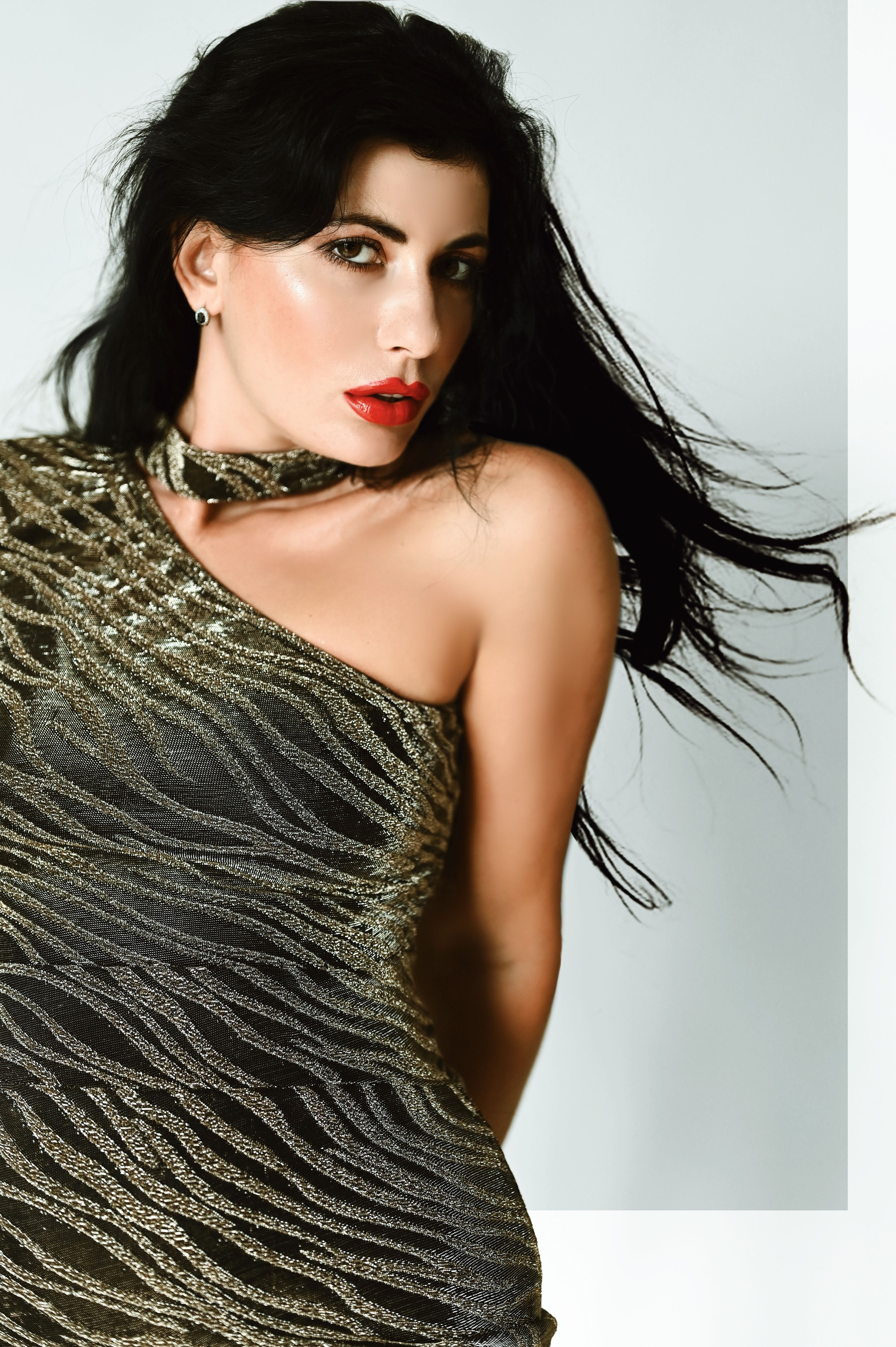 Glamorous portrait of a young woman posing in a shimmering dress, captured in a studio setting.