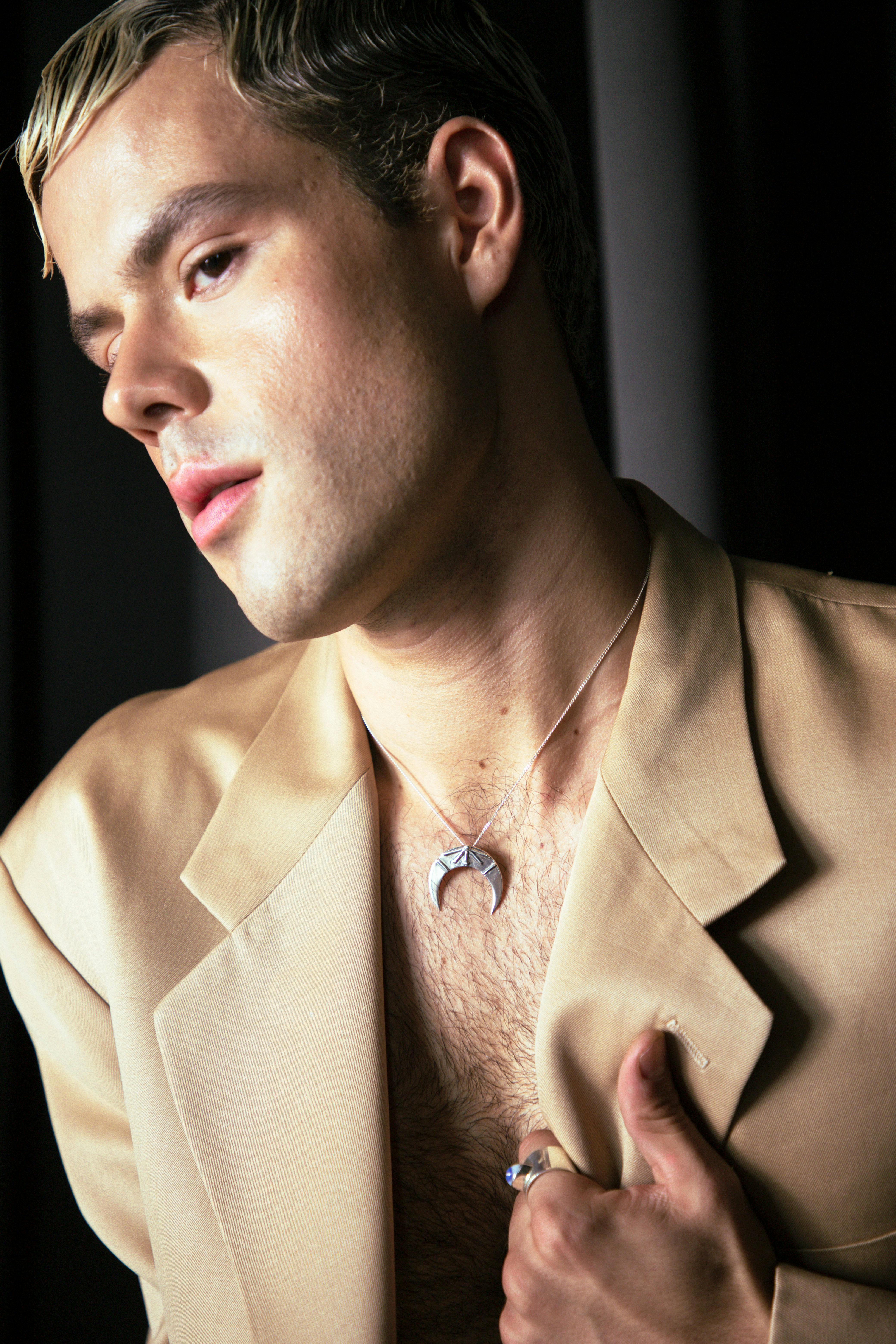 A close-up portrait of a man wearing a beige blazer with stylish accessories.