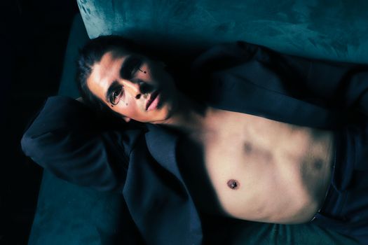 Stylish portrait of a man posing on a sofa with distinctive makeup and lighting.