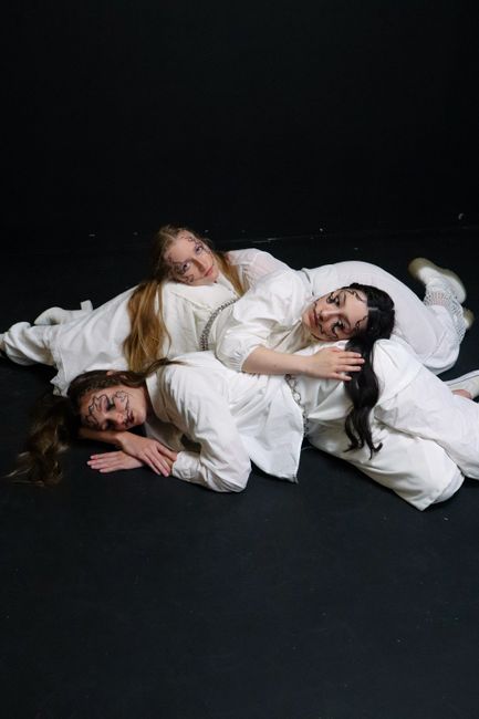 Creative studio portrait featuring three women in artistic white costumes lying on the floor.