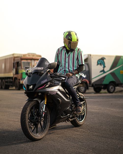 Free Man with helmet posing on a sportbike in Kannur, India, near colorful trucks. Stock Photo